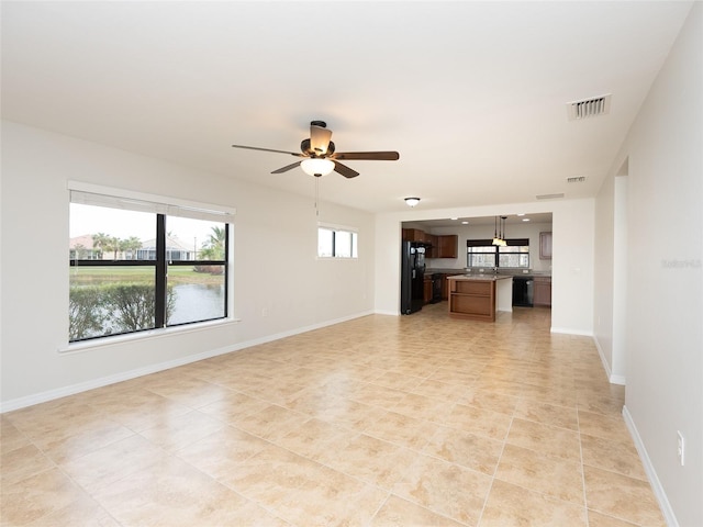 unfurnished living room with a water view, ceiling fan, and light tile patterned floors