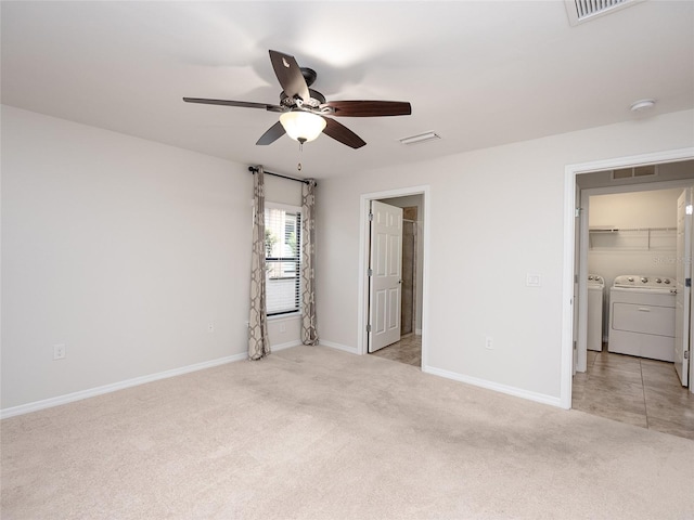 unfurnished bedroom featuring connected bathroom, a walk in closet, light colored carpet, ceiling fan, and washer and clothes dryer