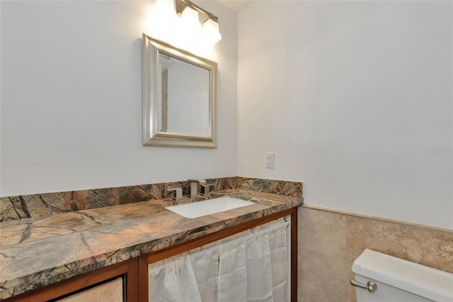 bathroom with toilet, vanity, and tile walls