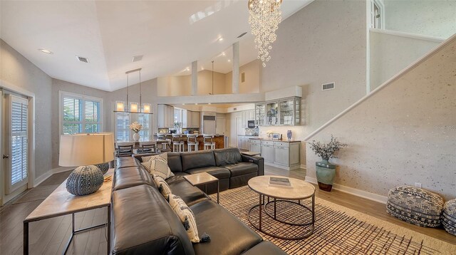 living room with an inviting chandelier, light hardwood / wood-style flooring, and high vaulted ceiling