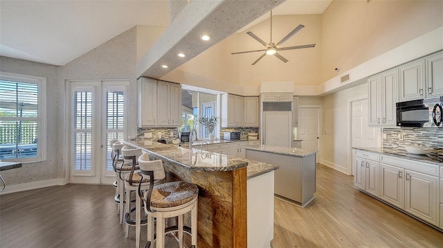 kitchen with a kitchen breakfast bar, paneled refrigerator, light stone countertops, a kitchen island, and decorative backsplash