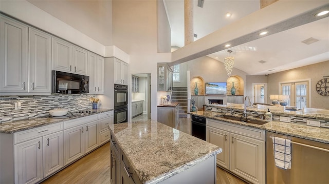 kitchen with sink, black appliances, light stone countertops, and a kitchen island