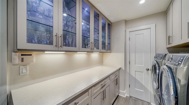 clothes washing area with cabinets, separate washer and dryer, and light hardwood / wood-style floors