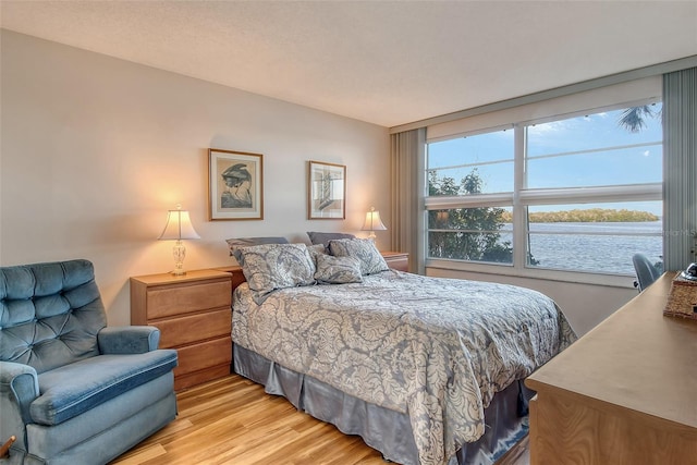 bedroom with light hardwood / wood-style floors and a water view