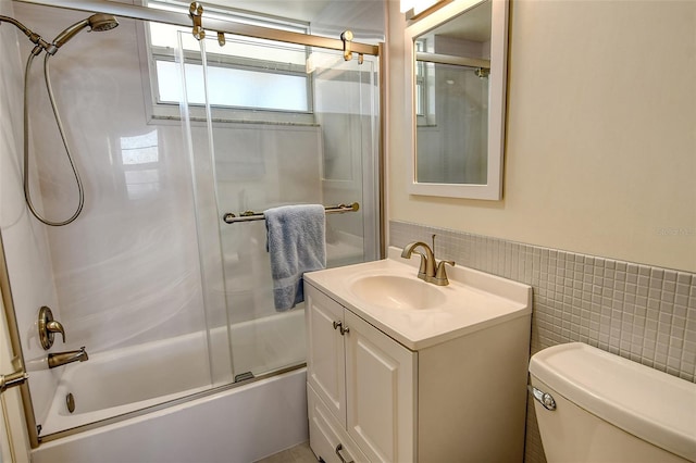 full bathroom with combined bath / shower with glass door, vanity, toilet, and tile walls