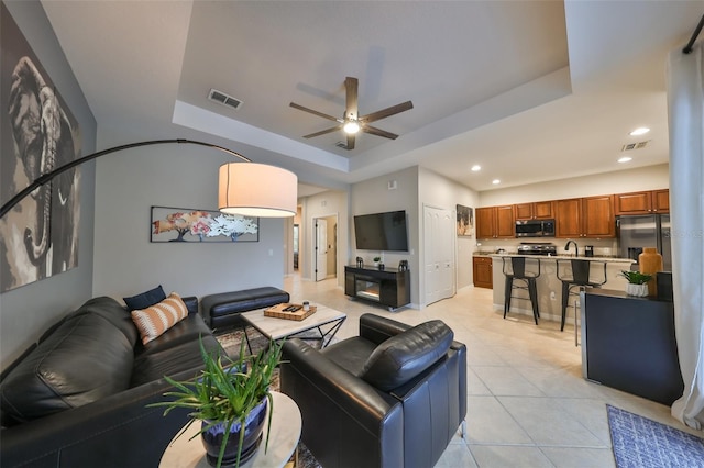 living room with ceiling fan, sink, light tile patterned flooring, and a tray ceiling