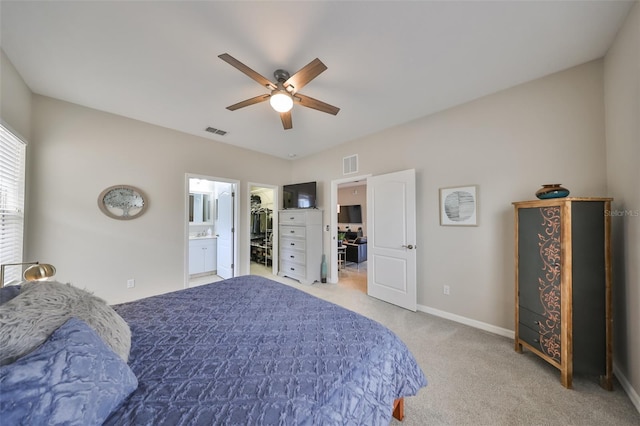 bedroom featuring ceiling fan, a walk in closet, light carpet, and ensuite bath