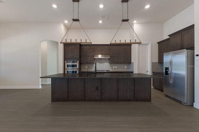 kitchen featuring a kitchen island with sink, hanging light fixtures, dark brown cabinets, and stainless steel appliances