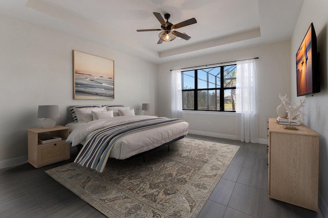 bedroom featuring ceiling fan, a tray ceiling, and dark tile patterned floors