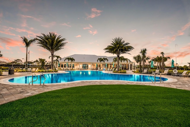 pool at dusk featuring a lawn and a patio area