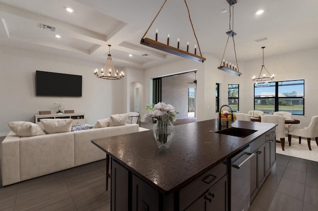 kitchen with an inviting chandelier, coffered ceiling, sink, and a center island with sink