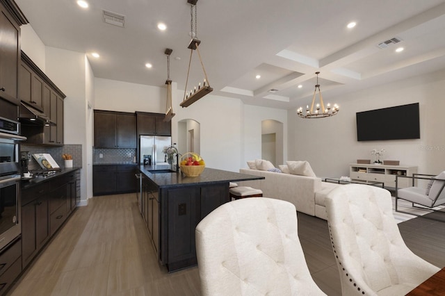 kitchen featuring appliances with stainless steel finishes, tasteful backsplash, an island with sink, coffered ceiling, and beam ceiling