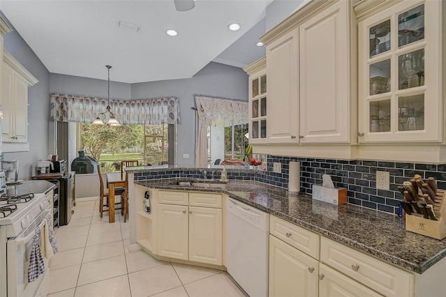 kitchen featuring decorative light fixtures, sink, dark stone counters, light tile patterned floors, and white appliances