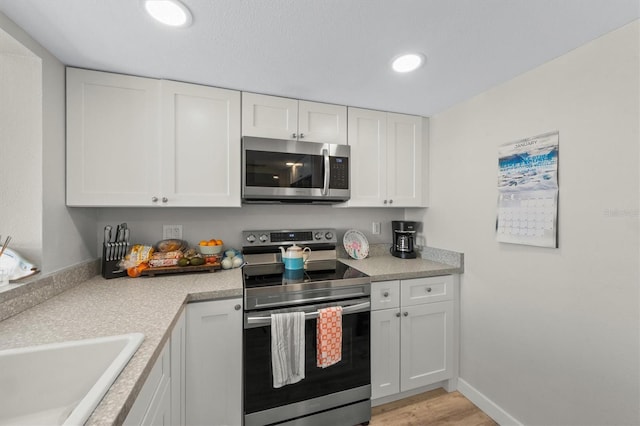 kitchen with light hardwood / wood-style flooring, sink, stainless steel appliances, and white cabinetry