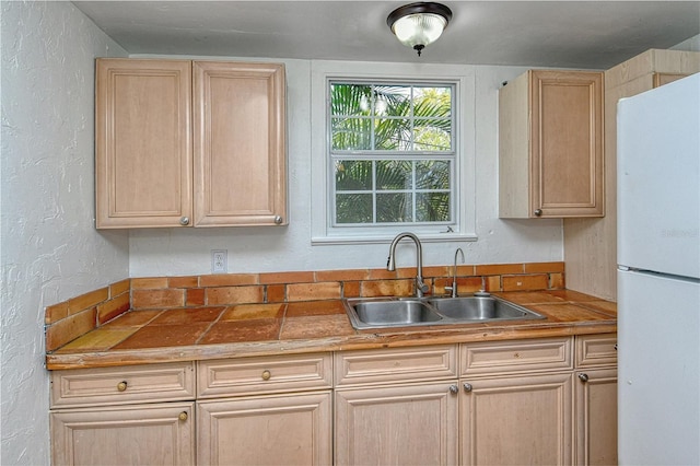 kitchen featuring light brown cabinetry, sink, and white refrigerator