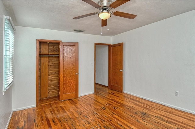 unfurnished bedroom featuring a textured ceiling, ceiling fan, a closet, and hardwood / wood-style flooring