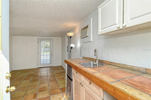 kitchen with tile patterned flooring, tile countertops, sink, a textured ceiling, and white cabinets