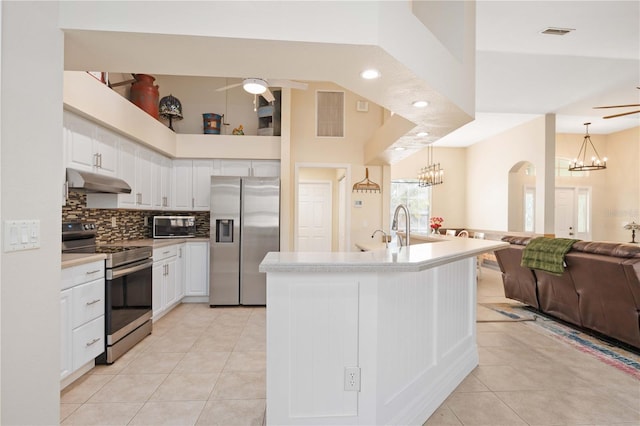 kitchen with ceiling fan with notable chandelier, appliances with stainless steel finishes, white cabinetry, an island with sink, and decorative light fixtures