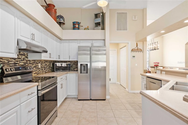 kitchen featuring appliances with stainless steel finishes, a towering ceiling, white cabinets, decorative backsplash, and light tile patterned floors