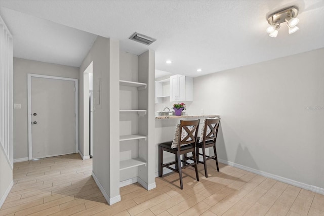 kitchen with a breakfast bar area, open shelves, visible vents, wood tiled floor, and white cabinets