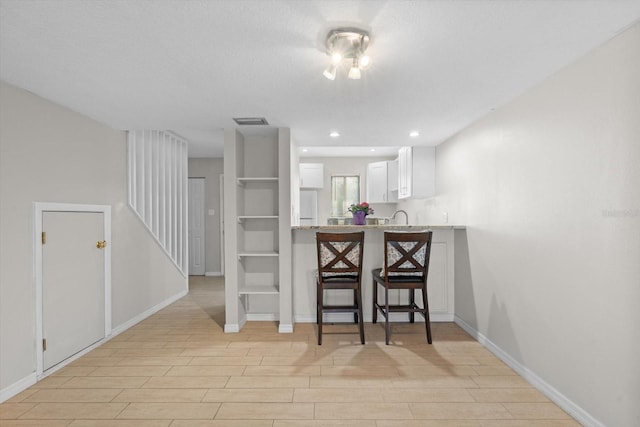 kitchen with visible vents, baseboards, light wood-style flooring, a kitchen breakfast bar, and white cabinetry