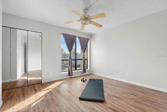 interior space featuring ceiling fan, a textured ceiling, baseboards, and wood finished floors