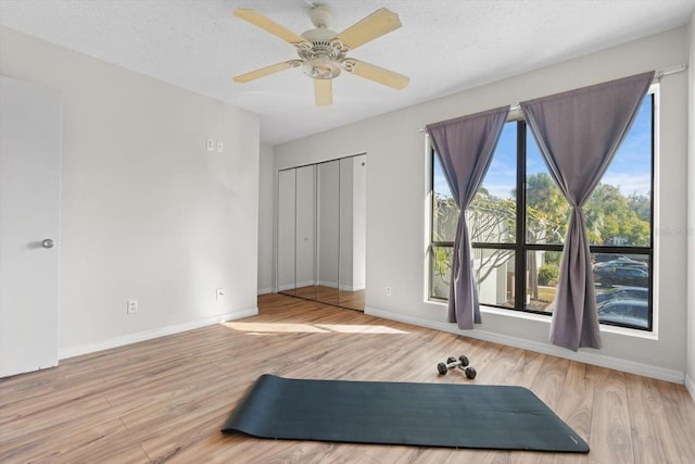 workout area featuring ceiling fan, a textured ceiling, baseboards, and wood finished floors