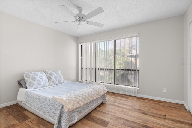 bedroom featuring ceiling fan, a textured ceiling, baseboards, and wood finished floors