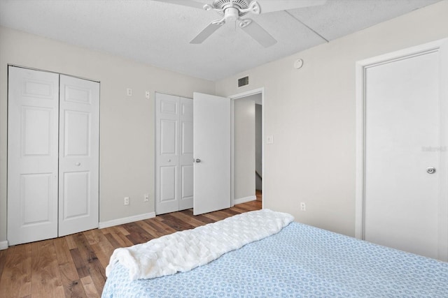 bedroom with ceiling fan, wood finished floors, visible vents, baseboards, and multiple closets