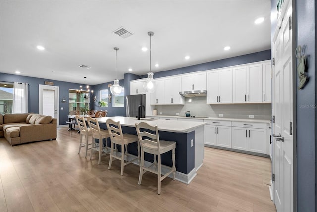 kitchen with stainless steel fridge, white cabinets, hanging light fixtures, black electric stovetop, and a center island with sink