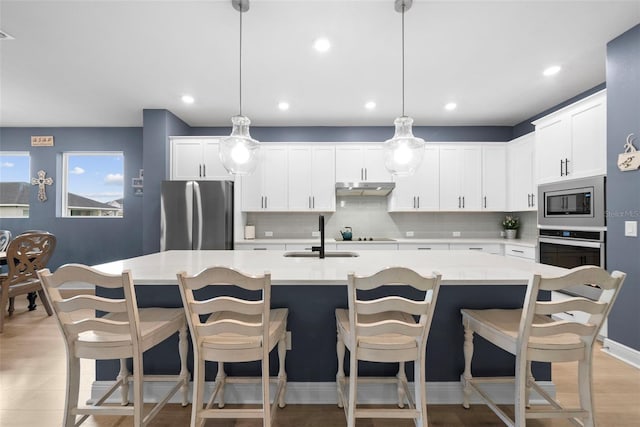 kitchen featuring stainless steel appliances, a center island with sink, sink, and pendant lighting