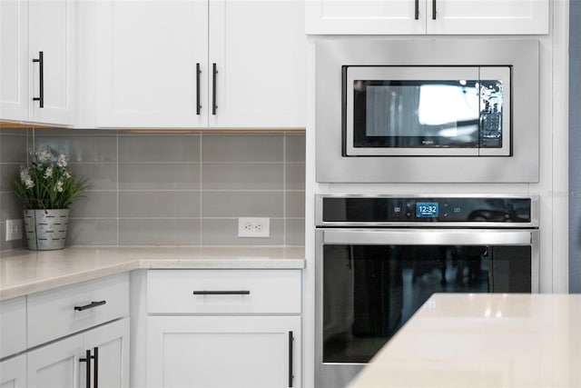 kitchen with light stone countertops, decorative backsplash, stainless steel appliances, and white cabinets