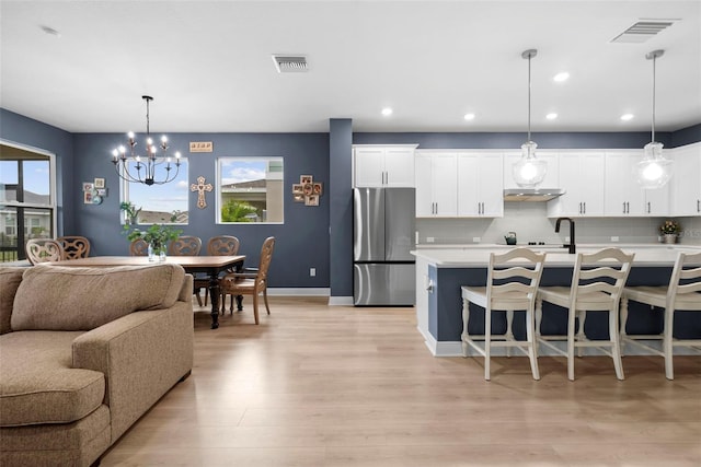 kitchen with pendant lighting, white cabinetry, stainless steel fridge, backsplash, and light hardwood / wood-style flooring