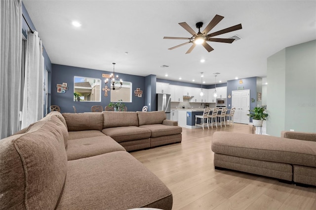 living room featuring ceiling fan with notable chandelier and light hardwood / wood-style floors