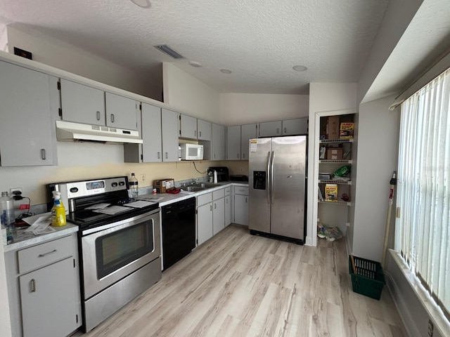 kitchen featuring gray cabinets, appliances with stainless steel finishes, light hardwood / wood-style floors, a textured ceiling, and lofted ceiling