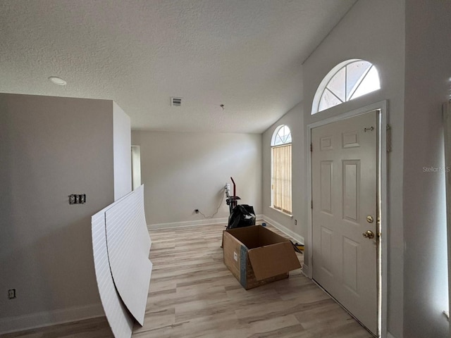 foyer with light wood-type flooring, vaulted ceiling, and a textured ceiling