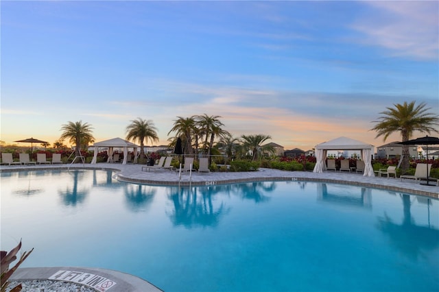 pool at dusk featuring a gazebo and a patio