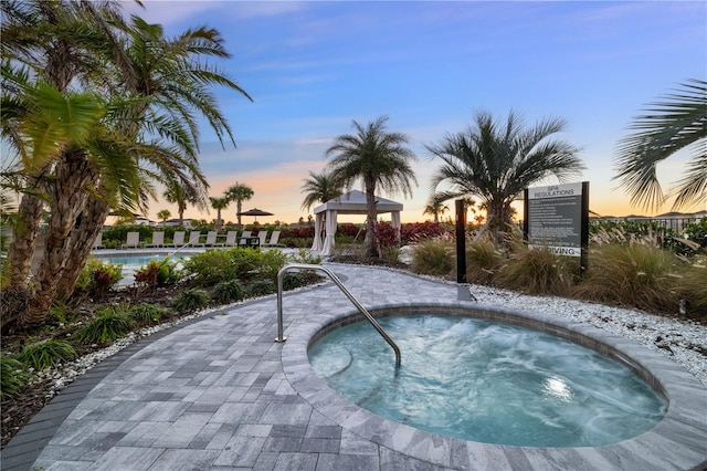 pool at dusk with a gazebo and a hot tub