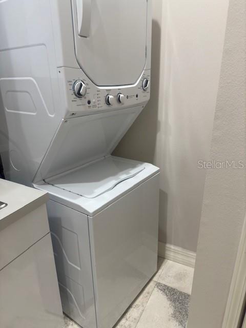 laundry area with cabinets, stacked washer / drying machine, and light tile patterned floors