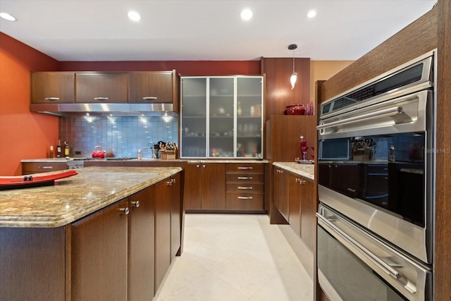 kitchen with backsplash, light stone countertops, pendant lighting, double oven, and dark brown cabinetry