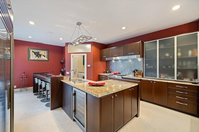 kitchen featuring a center island with sink, dark brown cabinets, wine cooler, hanging light fixtures, and sink