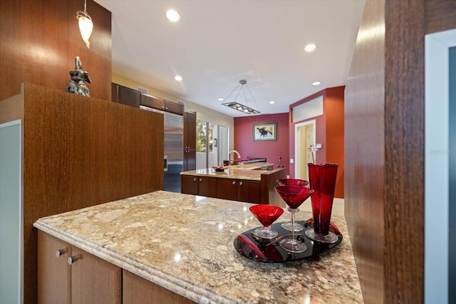 kitchen with light stone counters, a center island with sink, and hanging light fixtures