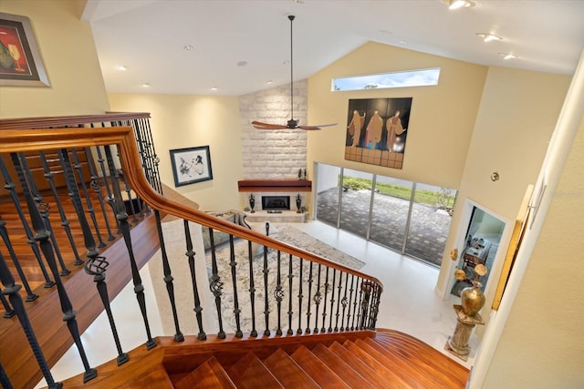 stairway featuring high vaulted ceiling, wood-type flooring, ceiling fan, and a fireplace