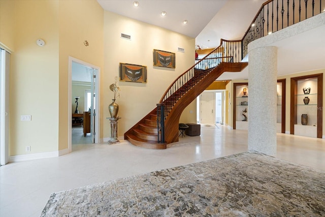 stairs with built in shelves, a high ceiling, and ornate columns