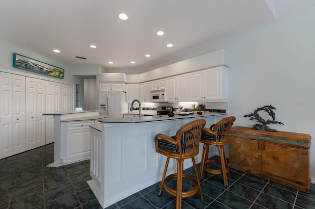 kitchen with refrigerator with ice dispenser, a kitchen island with sink, white cabinets, and sink