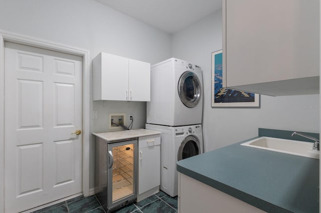 clothes washing area featuring stacked washer / dryer, beverage cooler, dark tile patterned floors, cabinets, and sink