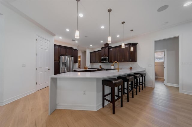 kitchen featuring appliances with stainless steel finishes, hanging light fixtures, light wood-type flooring, and kitchen peninsula