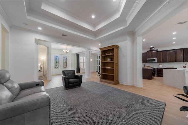 living room featuring crown molding, light hardwood / wood-style flooring, french doors, and a raised ceiling