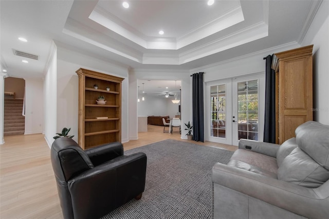 living room featuring a raised ceiling, ornamental molding, ceiling fan, french doors, and light hardwood / wood-style flooring