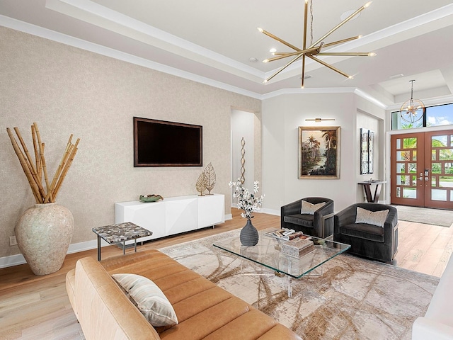 living room with a raised ceiling, light hardwood / wood-style flooring, a notable chandelier, and french doors